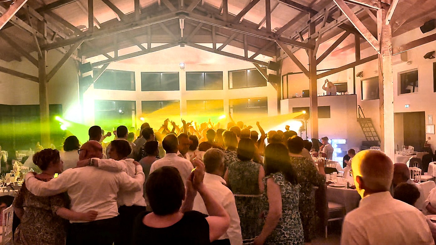 Piste de danse pleine lors d'un mariage, invités de tous âges les bras levés sous les projecteurs