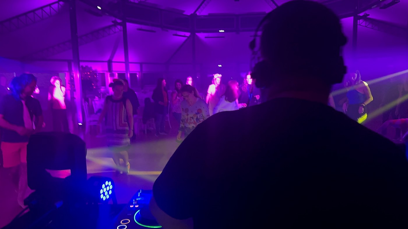 Deejay de mariage de dos derrière sa régie, casque sur les oreilles, observant les invités sur la piste de danse