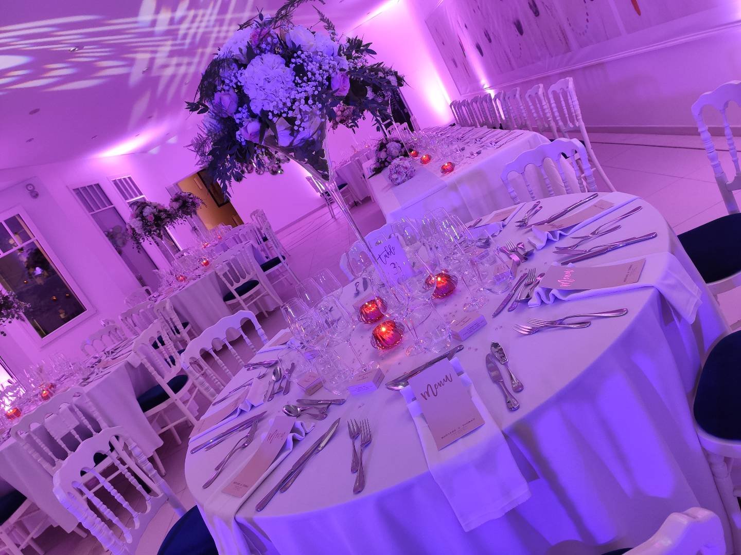 Table de mariage dressée avec centre de table fleuri sous un éclairage violet, Nord